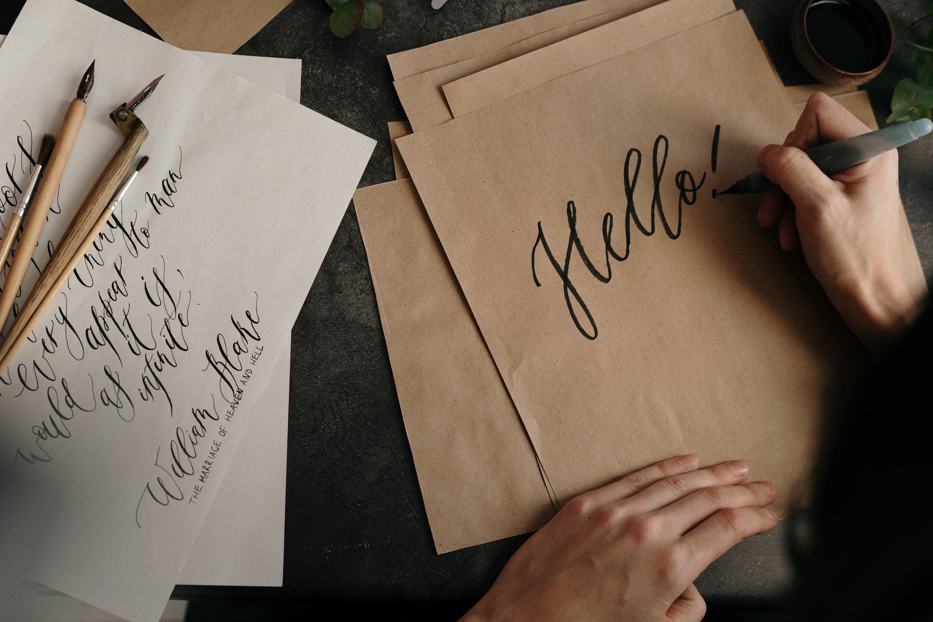 Hands writing the word Hello! on brown paper.